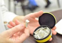 A hand holding a portion of snus with an open can in the background