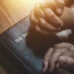 Two hands clasped in prayer over a Holy Bible