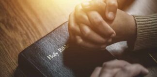 Two hands clasped in prayer over a Holy Bible