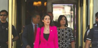 Group of individuals in formal attire exiting a building with security personnel