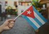A hand holding a small Cuban flag in an outdoor environment