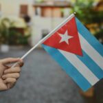 A hand holding a small Cuban flag in an outdoor environment