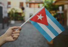 A hand holding a small Cuban flag in an outdoor environment