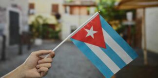 A hand holding a small Cuban flag in an outdoor environment