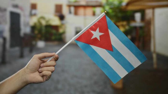 A hand holding a small Cuban flag in an outdoor environment