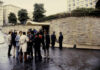 Group of people gathered outside a building with police officers nearby on a rainy day