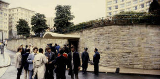 Group of people gathered outside a building with police officers nearby on a rainy day