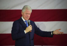 Man speaking with microphone in front of flag