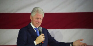 Man speaking with microphone in front of flag
