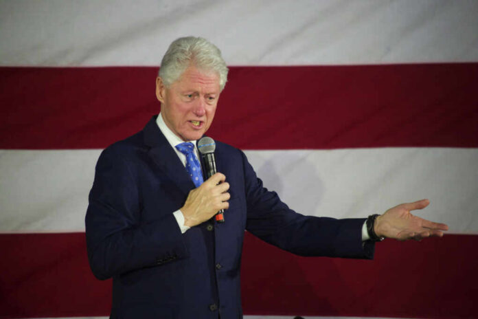Man speaking with microphone in front of flag