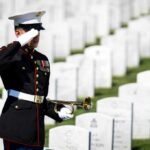 A soldier in uniform saluting in a military cemetery with white gravestones in the background