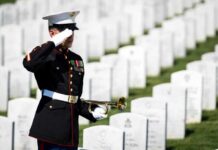 A soldier in uniform saluting in a military cemetery with white gravestones in the background
