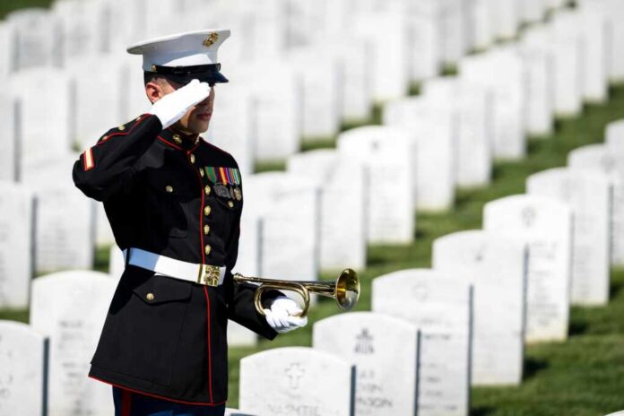 A soldier in uniform saluting in a military cemetery with white gravestones in the background