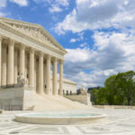 The U.S. Supreme Court building with a fountain in the foreground under a blue sky