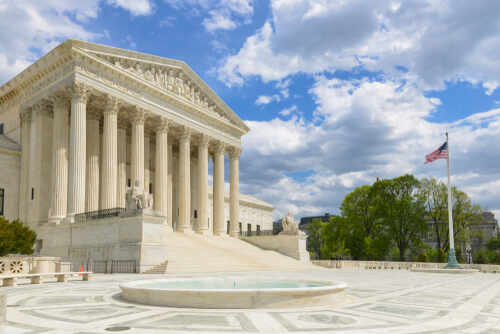 The U.S. Supreme Court building with a fountain in the foreground under a blue sky