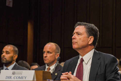Government officials seated during a hearing with a nameplate in front of one