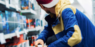 A young man in a colorful jacket crouching in a retail store aisle