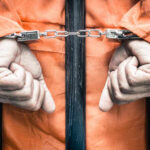 Healthcare Scam: Ex-NFL Player’s 16-Year Sentence Hands of a prisoner in orange jumpsuit secured with handcuffs behind bars