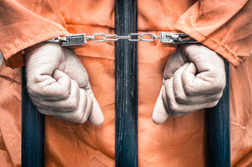 Hands of a prisoner in orange jumpsuit secured with handcuffs behind bars