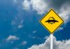 A yellow caution sign depicting a UFO against a blue sky with clouds