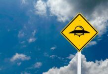 A yellow caution sign depicting a UFO against a blue sky with clouds
