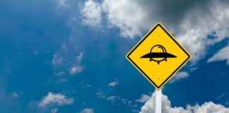 A yellow caution sign depicting a UFO against a blue sky with clouds