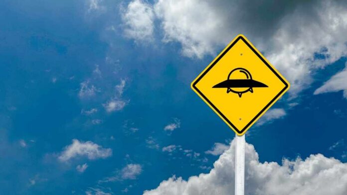 shutterstock_2318876455.jpg A yellow caution sign depicting a UFO against a blue sky with clouds