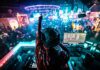 A DJ performing in a vibrant nightclub filled with dancing people