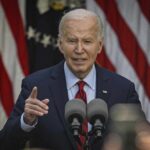 A man speaking at a podium with microphones in front of American flags