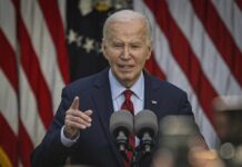 A man speaking at a podium with microphones in front of American flags