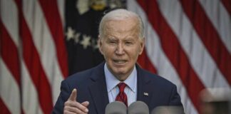 A man speaking at a podium with microphones in front of American flags