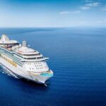 Hantavirus Hits Cruise – Five States On Edge A large cruise ship sailing on a calm ocean under a clear blue sky