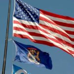 American flag and Michigan state flag flying against a blue sky