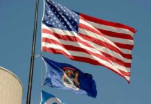 American flag and Michigan state flag flying against a blue sky