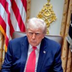 White House UFO Tease Morphs Into ICE Donald Trump seated in the Oval Office with a serious expression