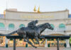 Bronze statue of a jockey riding a horse in front of Churchill Downs