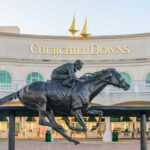 Bronze statue of a jockey riding a horse in front of Churchill Downs