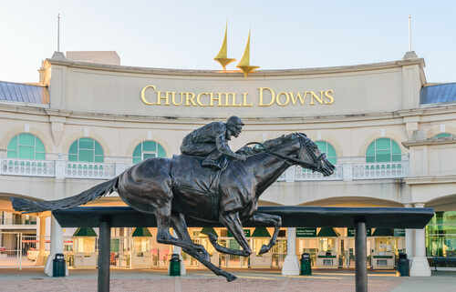 Bronze statue of a jockey riding a horse in front of Churchill Downs