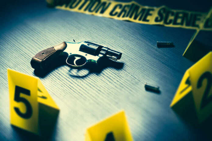 A handgun on a table with evidence markers and crime scene tape in the background