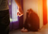 Person with clenched fist confronting a curled-up figure.