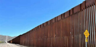 Tall border fence beside a dirt road desert