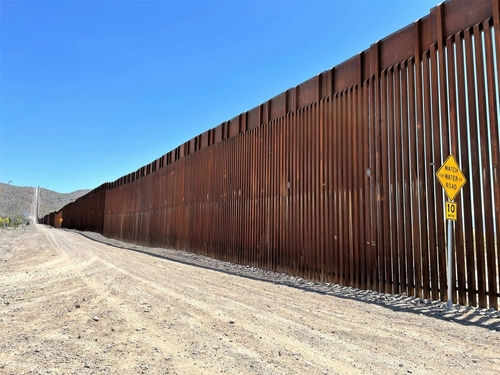 border-wall-2450843609 Tall border fence beside a dirt road desert