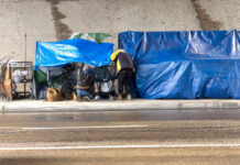 Homeless Voters Paid, Feds Say Two people at a sidewalk encampment with blue tarps and carts