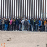 Large group of people standing near border fence
