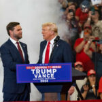 2028 Mind Game: Trump Dangles Two Names Two men in suits on stage at a crowded political rally