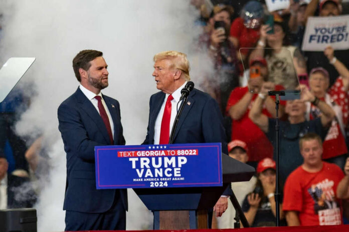 jdvanceid2499200129jpg Two men in suits on stage at a crowded political rally
