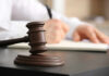 Wooden judge's gavel on a desk with a person writing in the background
