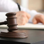 Battery Charge Sparks Judicial Meltdown Wooden judge's gavel on a desk with a person writing in the background