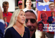 Woman speaking at outdoor event with protest signs in background