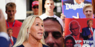 Woman speaking at outdoor event with protest signs in background